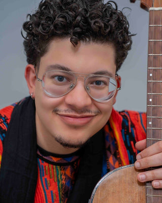 Person holding a wooden guitar with a colorful shirt and glasses